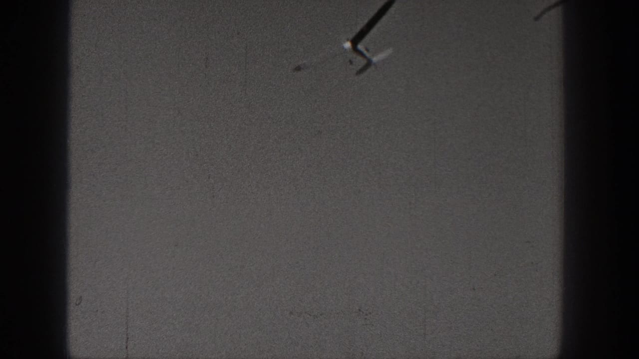 Distant small airplane in a Washington 1938 8mm home-movie sky shot with heavy grain and dark borders.