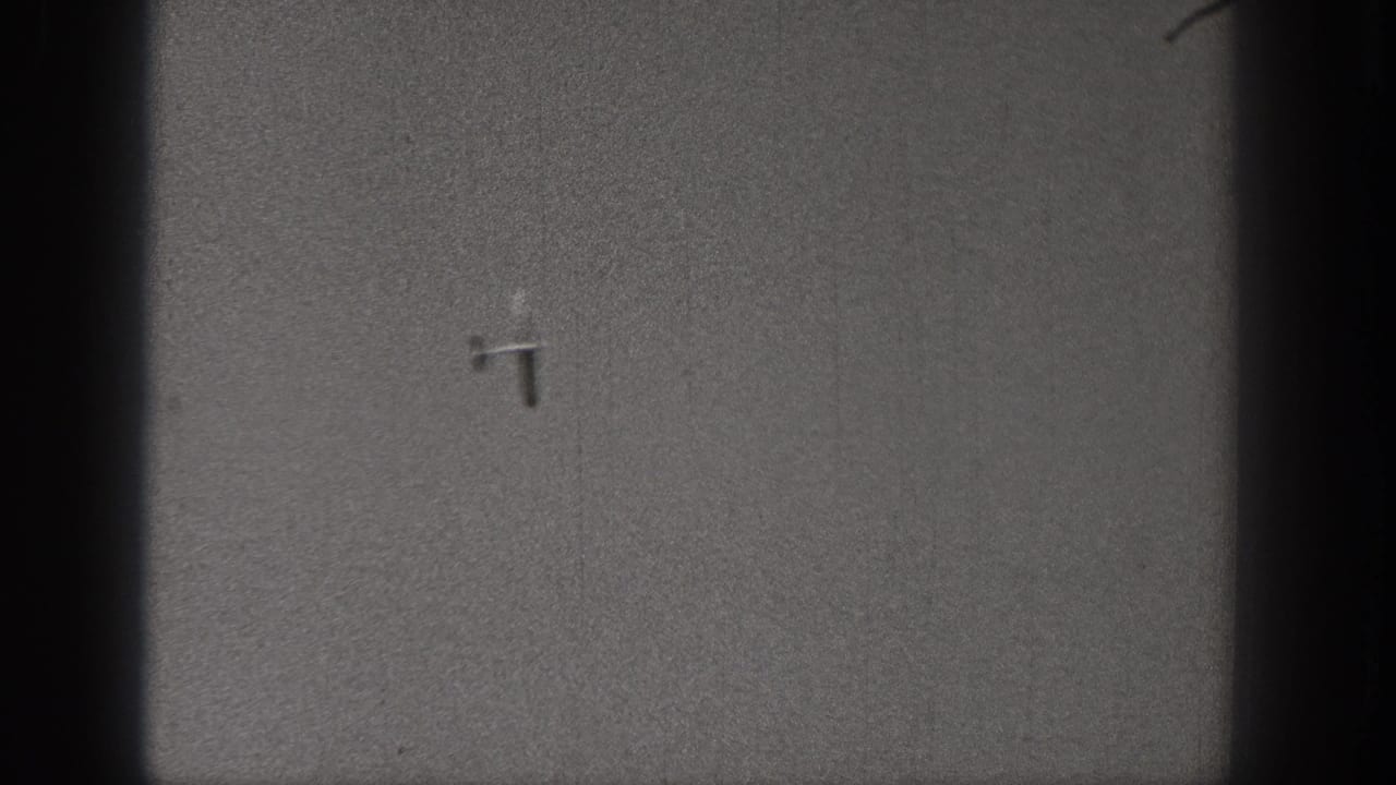 Small model airplane near the upper center of a grainy gray sky frame.