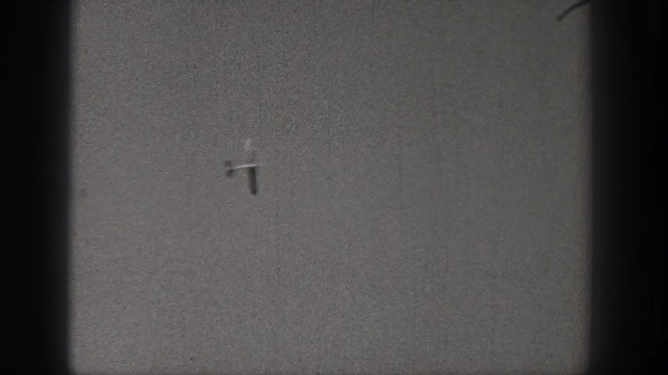 Small model airplane silhouetted in a gray Washington sky, recorded on grainy black-and-white 8mm footage.