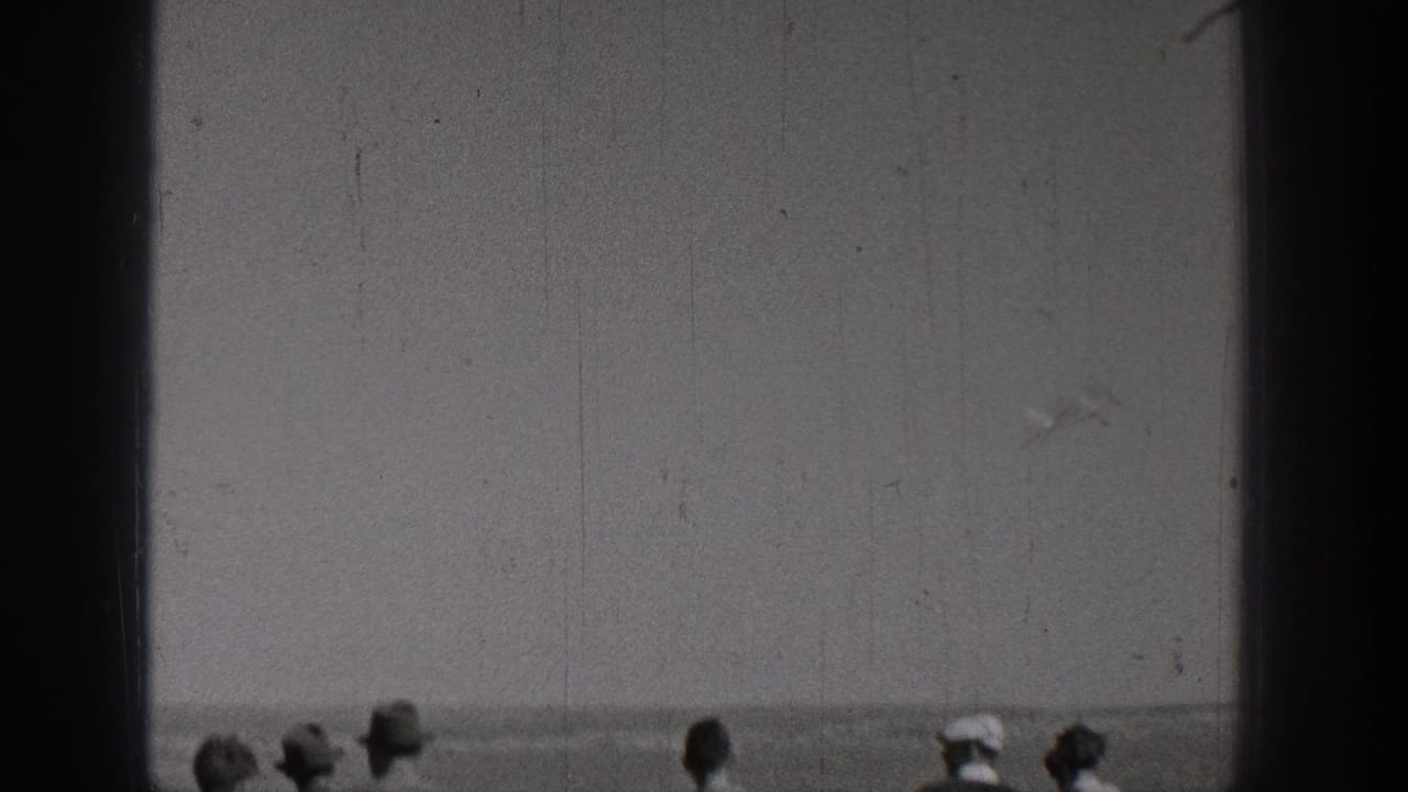 Distant spectator heads along the lower edge beneath an open sky or field view.