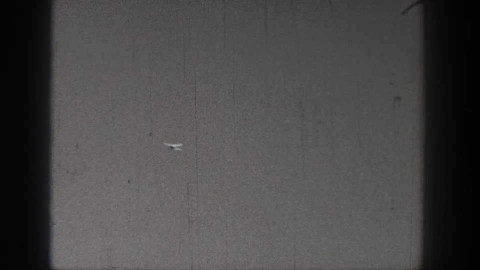 1938 Washington home-movie frame where a tiny model aircraft appears low in a largely empty outdoor view.