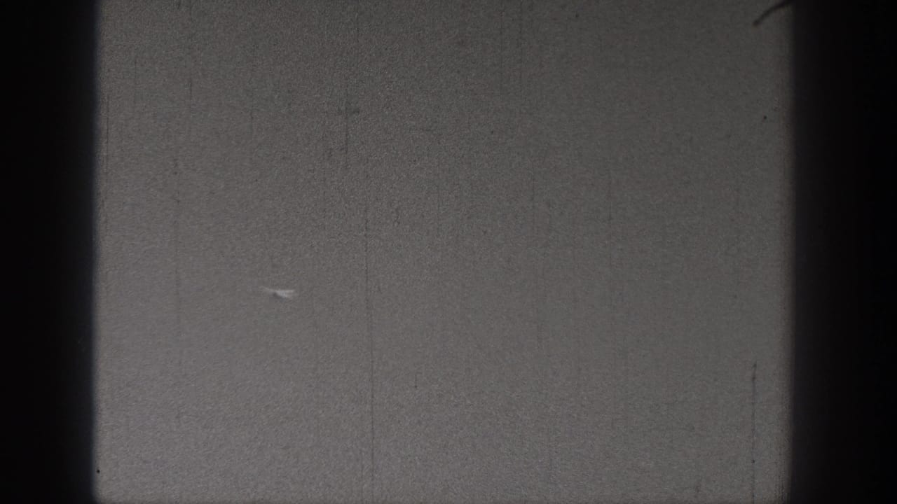 A distant model airplane appears against a gray sky in 1938 Washington 8mm home-movie footage, with heavy grain and dark frame edges.