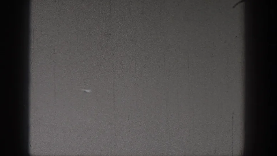 A distant model airplane appears against a gray sky in 1938 Washington 8mm home-movie footage, with heavy grain and dark frame edges.