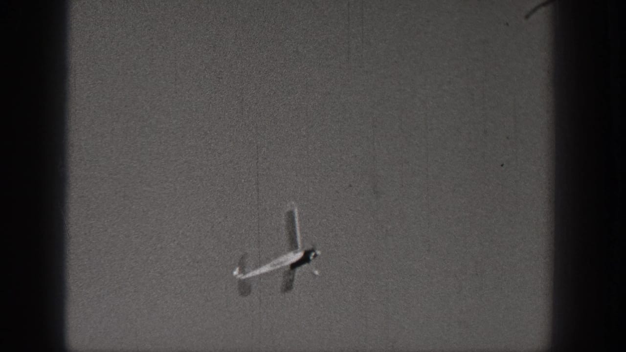 Distant model airplane angled in flight against a plain sky.