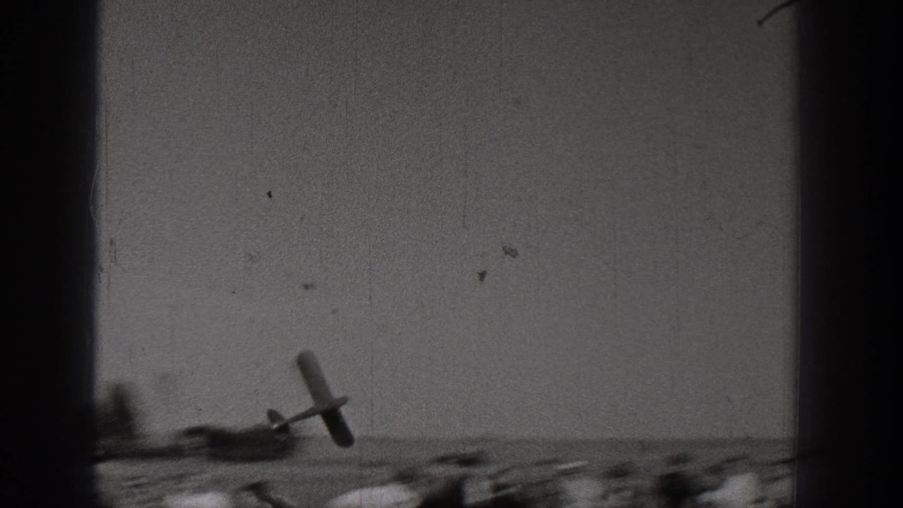 1938 Washington 8mm frame with a small model airplane flying low over a sparse sandy landscape.