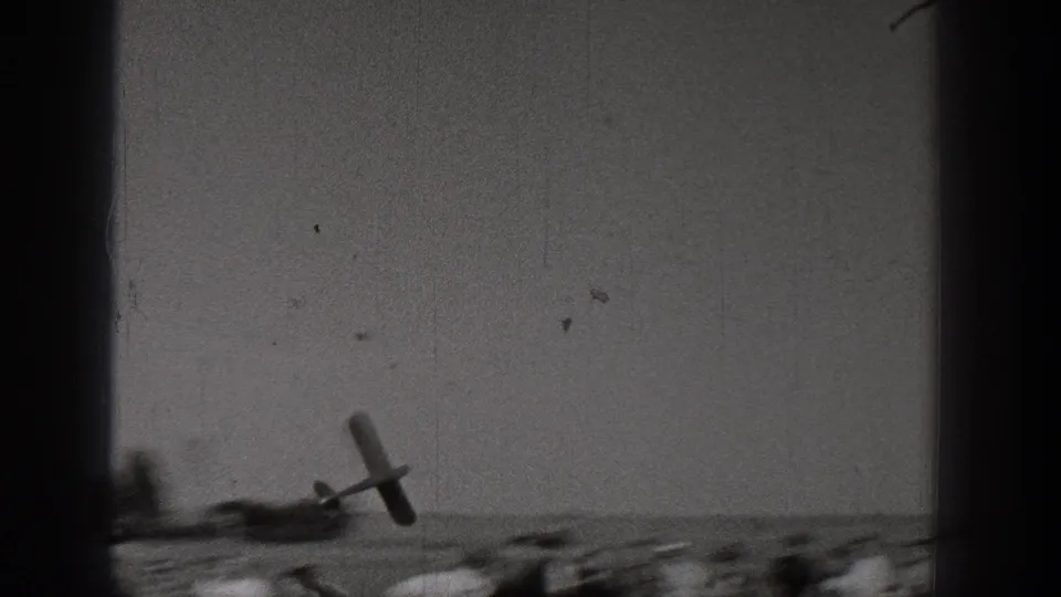 1938 Washington 8mm frame with a small model airplane flying low over a sparse sandy landscape.