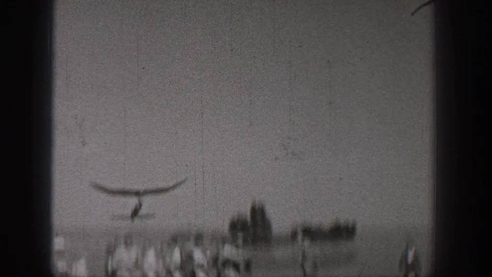 1938 Washington home-movie frame showing a small glider overhead with men gathered below in a rural field.