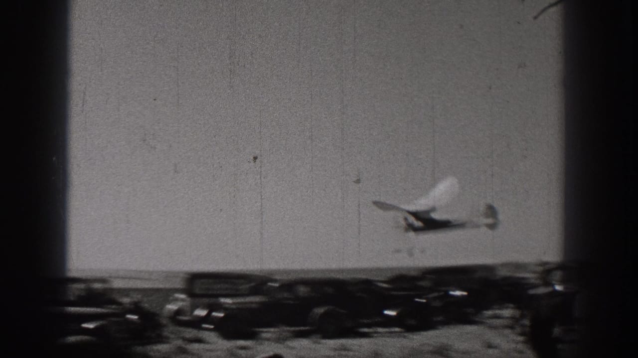 1938 Washington home-movie frame showing the small glider flying low above parked cars and an open field.