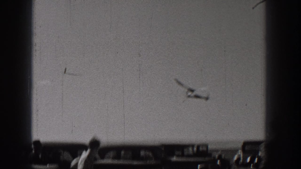 In Washington, United States, 1938, a radio-controlled model airplane appears in flight above parked cars and a few spectators.