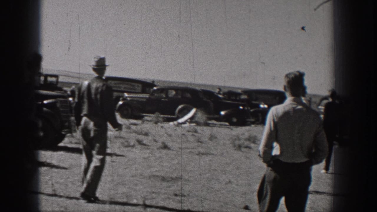 Men in period clothing move across an open field near vintage automobiles during the Washington radio-control plane test.