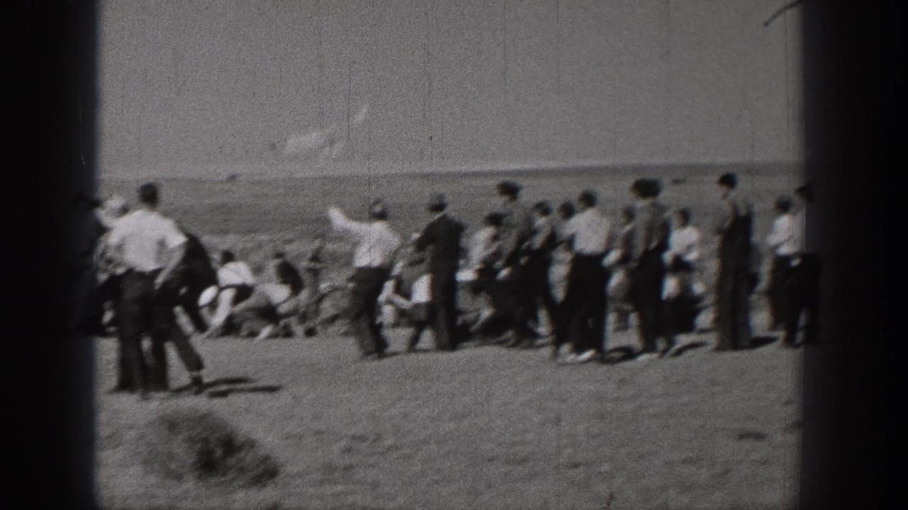 Washington 1938 home-movie frame showing a distant outdoor group gathered on open ground, with several figures looking toward the sky or horizon.