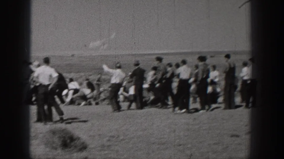 Washington 1938 home-movie frame showing a distant outdoor group gathered on open ground, with several figures looking toward the sky or horizon.