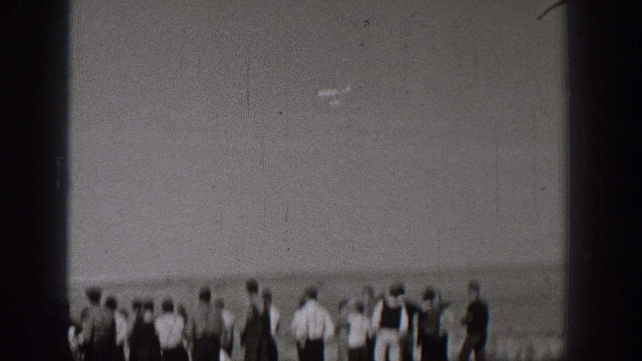 A group of people stands along a waterfront, seen through dark film-edge borders.