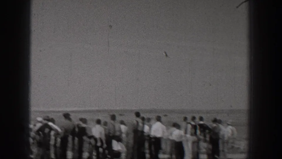 A 1938 Washington home-movie frame shows adults gathered beside the water, watching something beyond the camera's view.