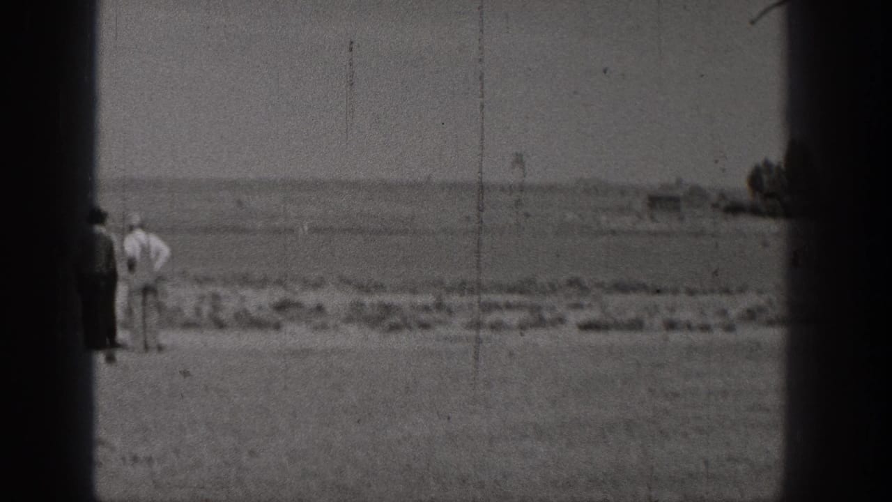 The closing 8mm frame shows people on open ground by the water in Washington, with distant shoreline and rocks visible through soft focus.