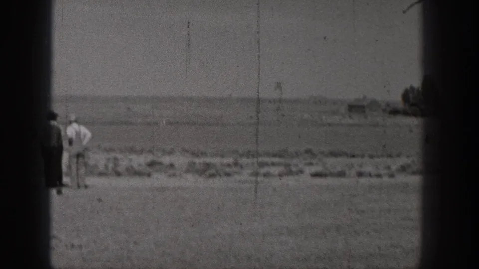 The closing 8mm frame shows people on open ground by the water in Washington, with distant shoreline and rocks visible through soft focus.