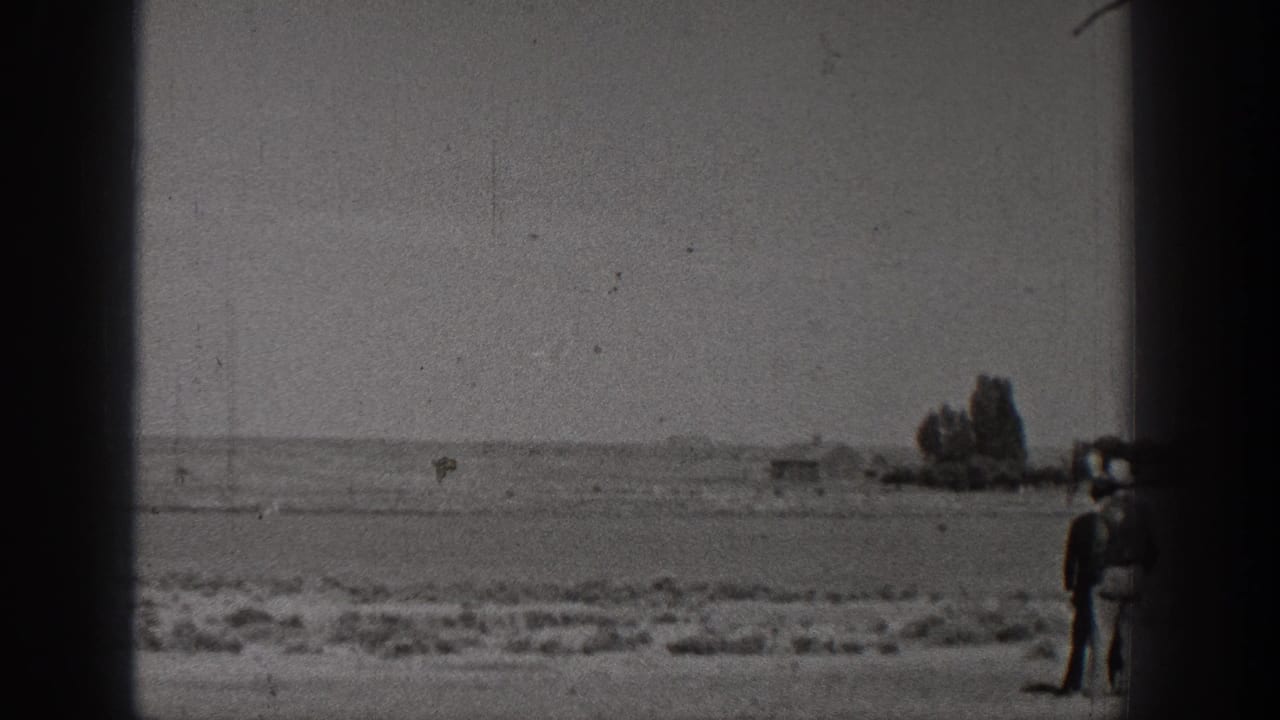 1938 Washington home-movie frame with a small aircraft near the horizon over open rural ground and heavy 8mm frame borders.