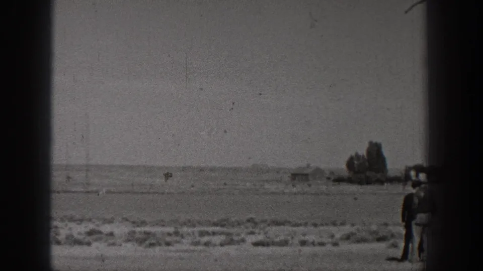 1938 Washington home-movie frame with a small aircraft near the horizon over open rural ground and heavy 8mm frame borders.