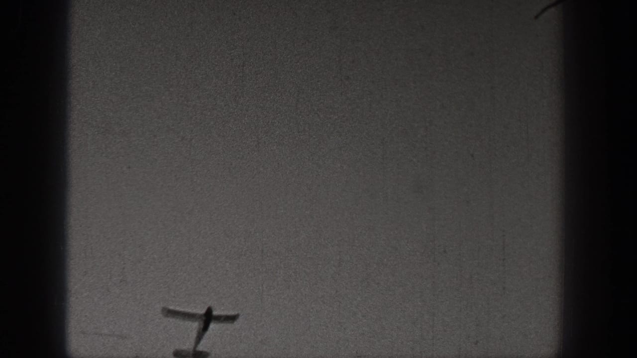Small training aircraft filmed against a blank gray sky in a grainy 1938 Washington 8mm frame.