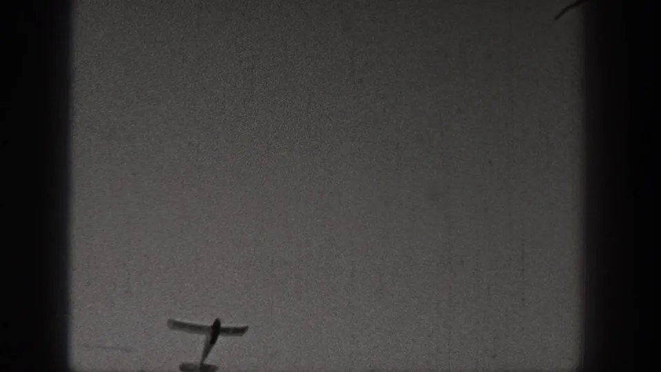Small training aircraft filmed against a blank gray sky in a grainy 1938 Washington 8mm frame.