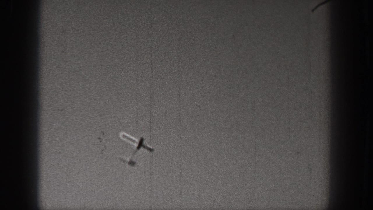 A small aircraft appears tilted in flight within a dark-bordered 1938 Washington 8mm home-movie frame.