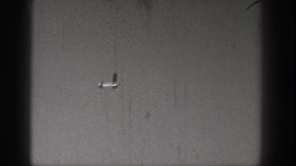 Small light aircraft viewed against a gray sky in a scratched, grainy 1938 Washington 8mm frame.