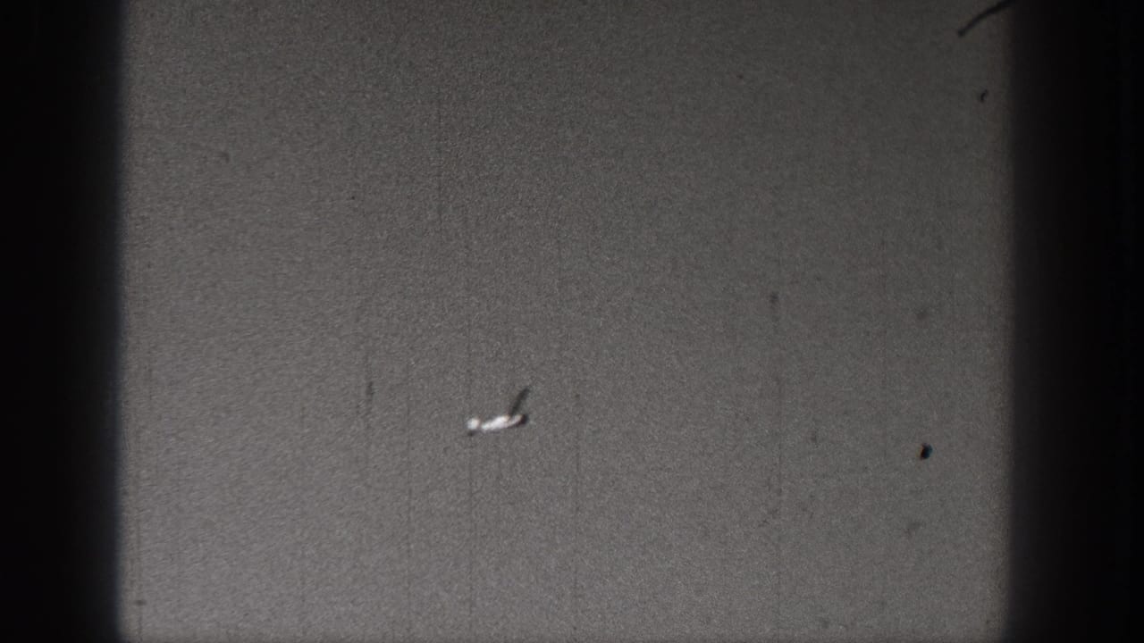 A small plane or model aircraft appears in the sky over an open Washington landscape in 1938 home-movie footage.