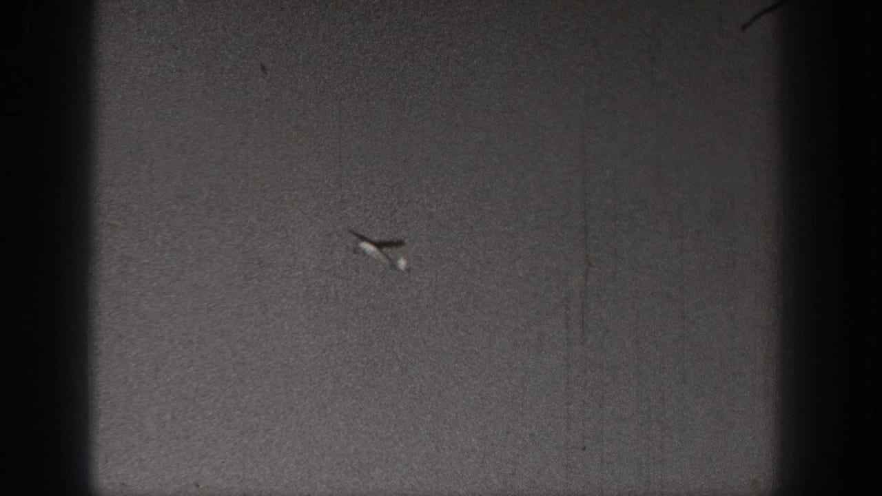 A small plane or model aircraft is isolated against the grainy sky near the end of the short home-movie clip.