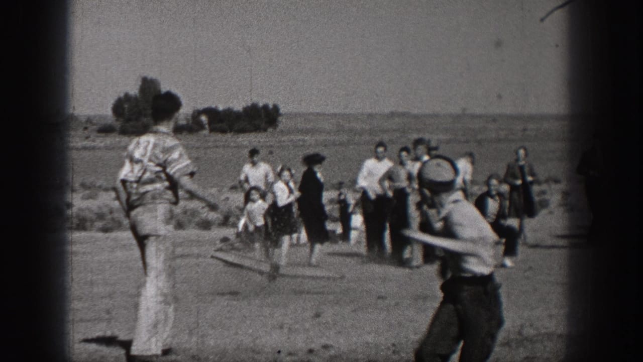 1938 Washington home-movie frame showing children and adults gathered in an open field, with a boy holding a bat near the camera.