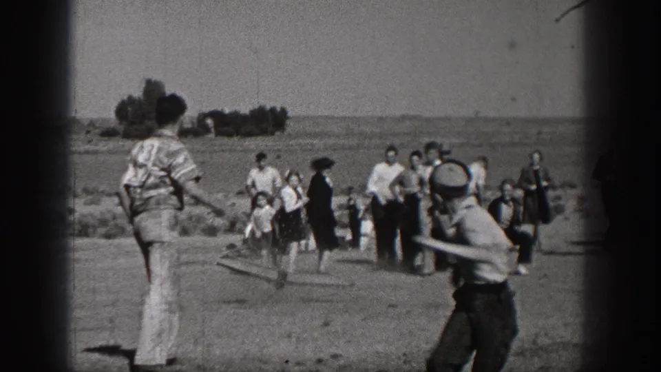 1938 Washington home-movie frame showing children and adults gathered in an open field, with a boy holding a bat near the camera.