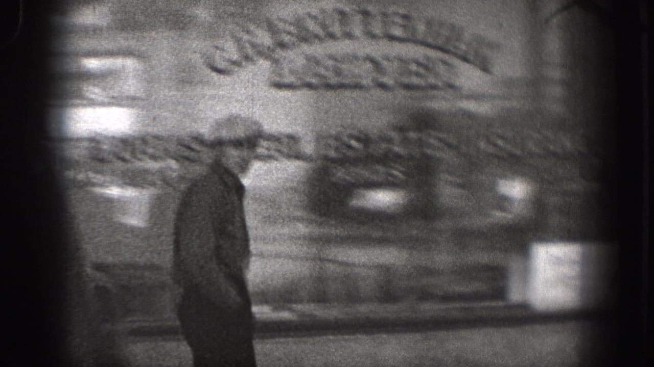 A man in a hat walks past a blurred storefront or street-facing building.