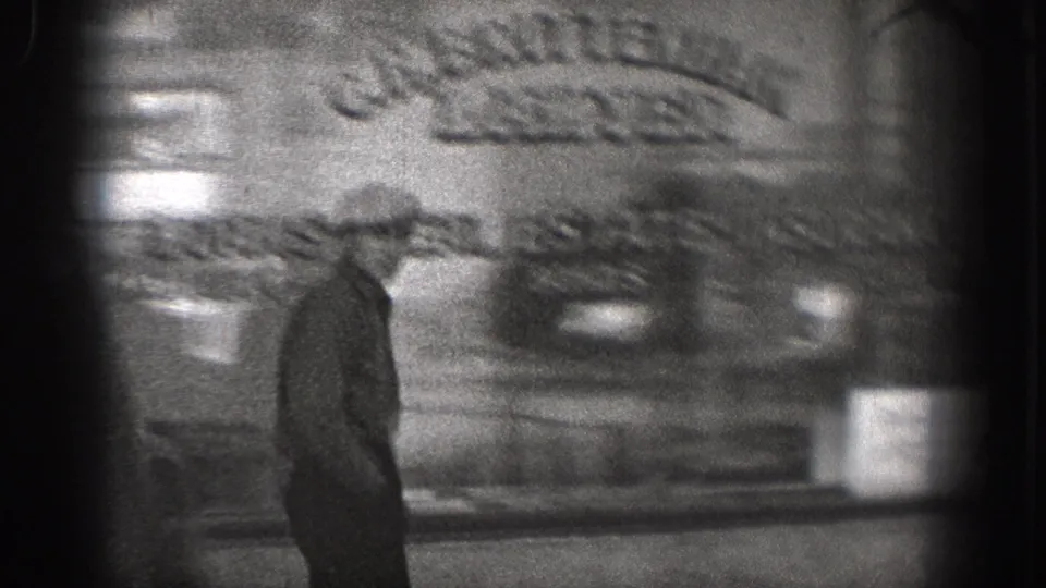Soft black-and-white frame of a man in a brimmed hat walking past a street-facing building in Washington, 1938.