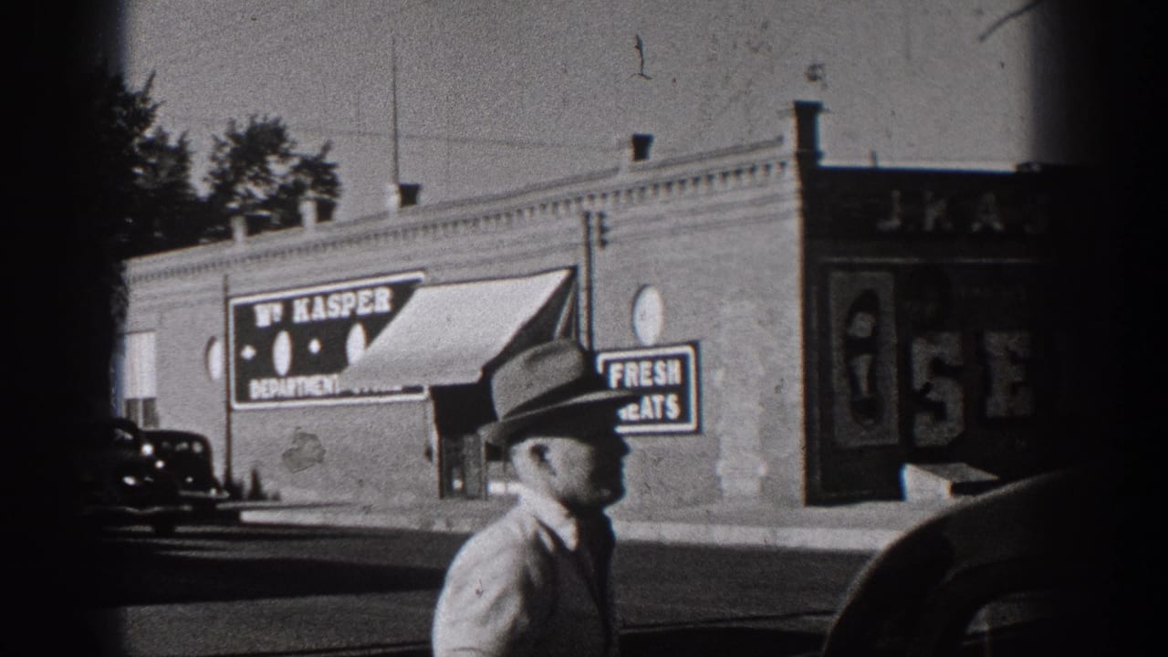 1938 Washington street frame with a man in a hat near brick storefronts, W. Kasper signage, painted window signs, and a parked car.