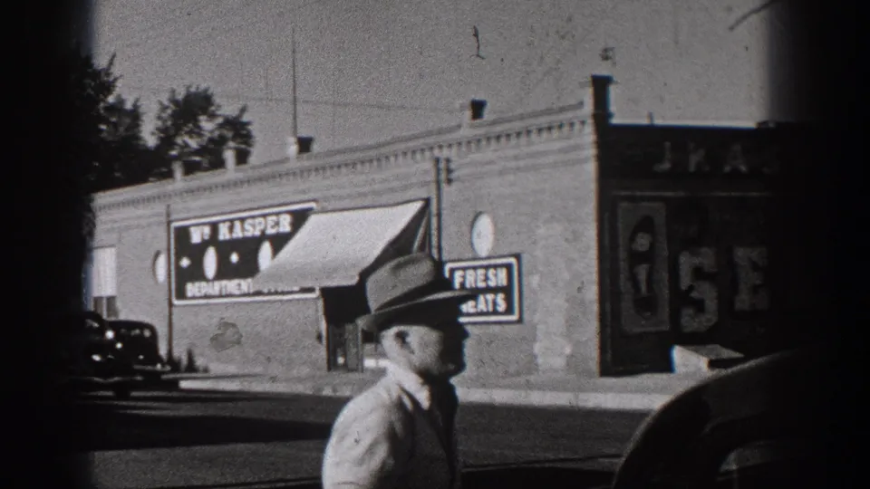 1938 Washington street frame with a man in a hat near brick storefronts, W. Kasper signage, painted window signs, and a parked car.