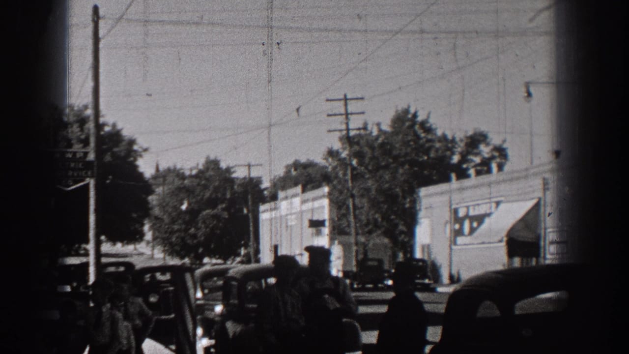 1938 Washington small-town street view with vintage automobiles, storefronts, trees, and overhead utility lines in black-and-white 8mm footage.