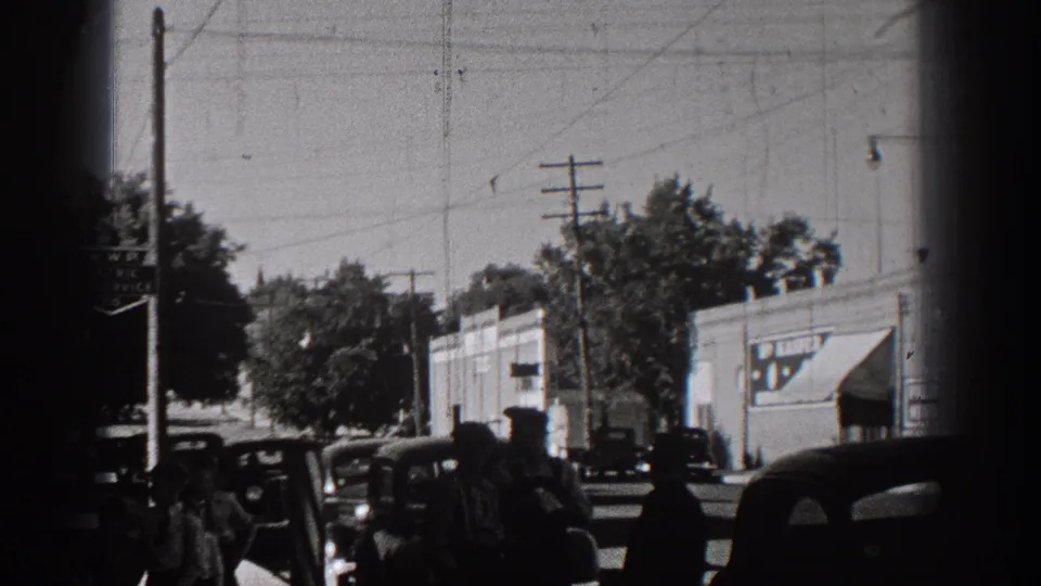 1938 Washington small-town street view with vintage automobiles, storefronts, trees, and overhead utility lines in black-and-white 8mm footage.
