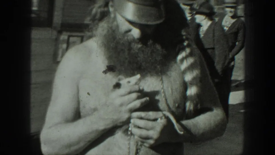 The bearded man looks down while holding the small animal against his chest in the 1939 California home-movie scene.