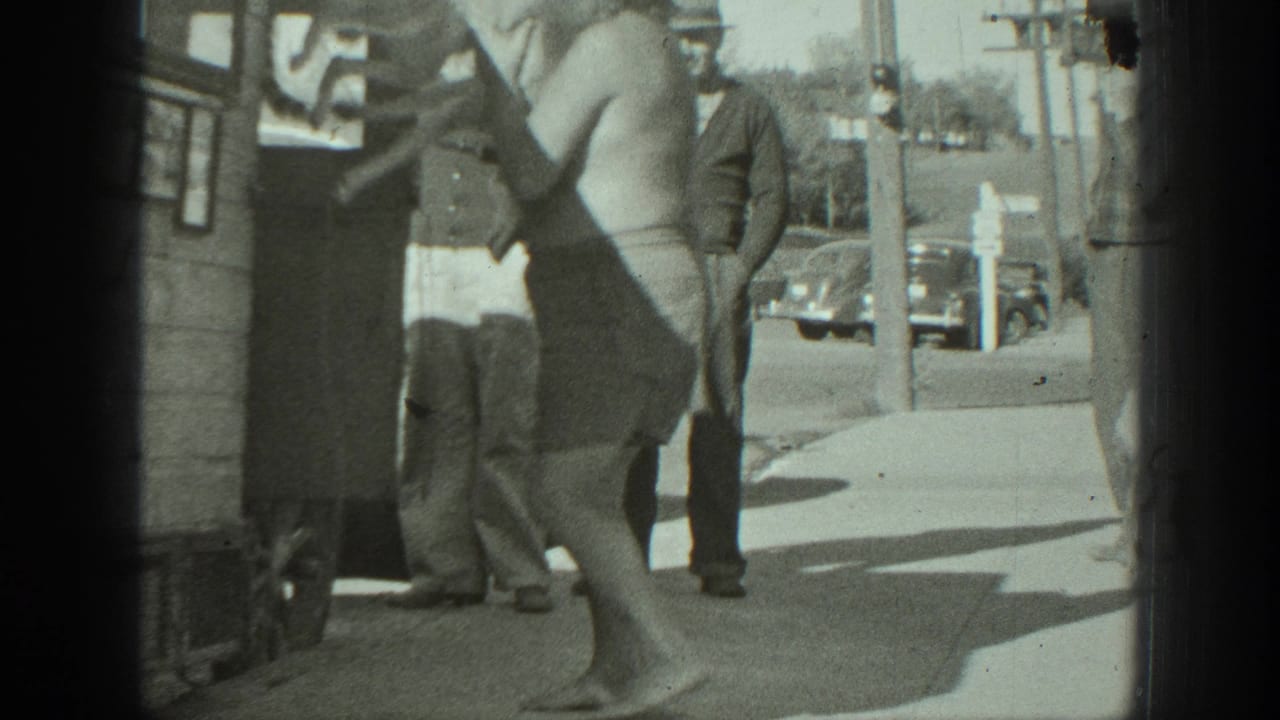 Man in shorts carries a dog away from a vehicle while several men watch nearby.