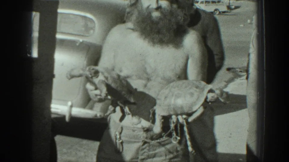 A closer 1939 California frame shows the bearded man holding a turtle in each hand, with a parked car and street behind him.