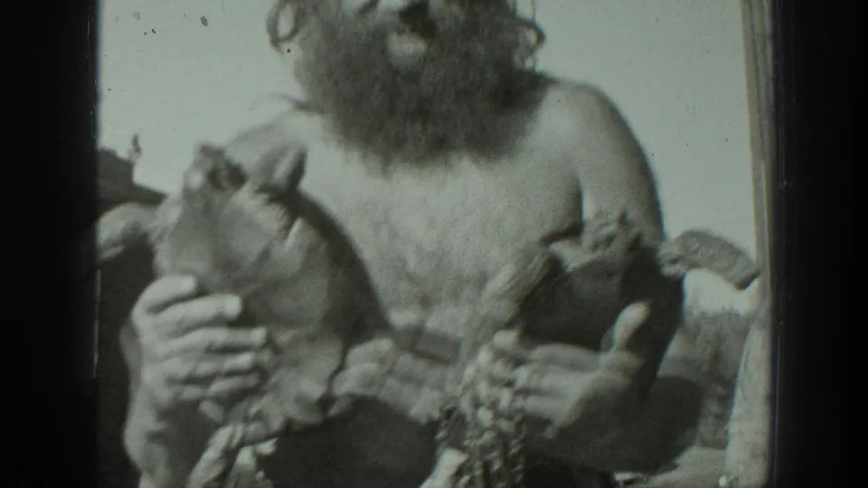 The 8mm frame moves closer to the man’s chest and hands, emphasizing the two turtles he is holding toward the camera.