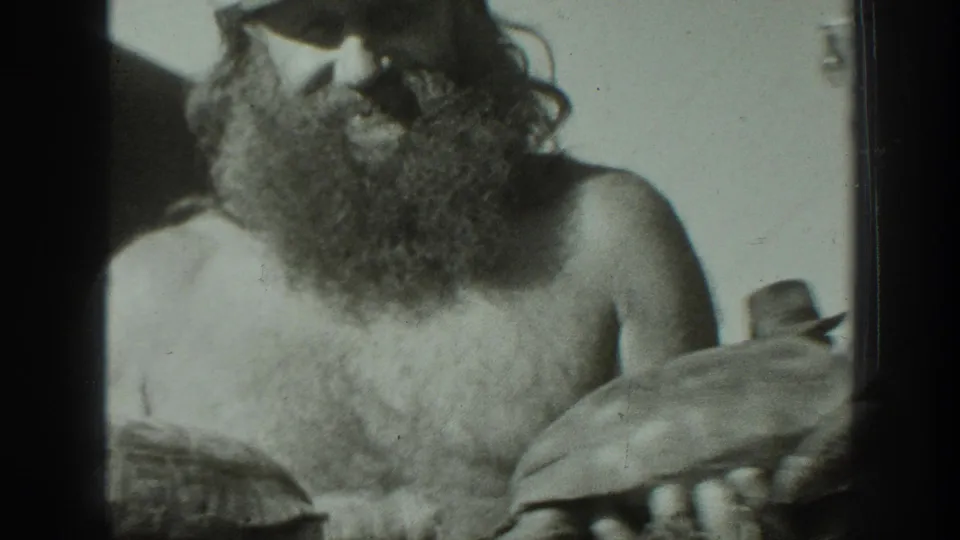 In 1939 California home-movie footage, a bearded man wearing a cap holds a tortoise while facing the camera.