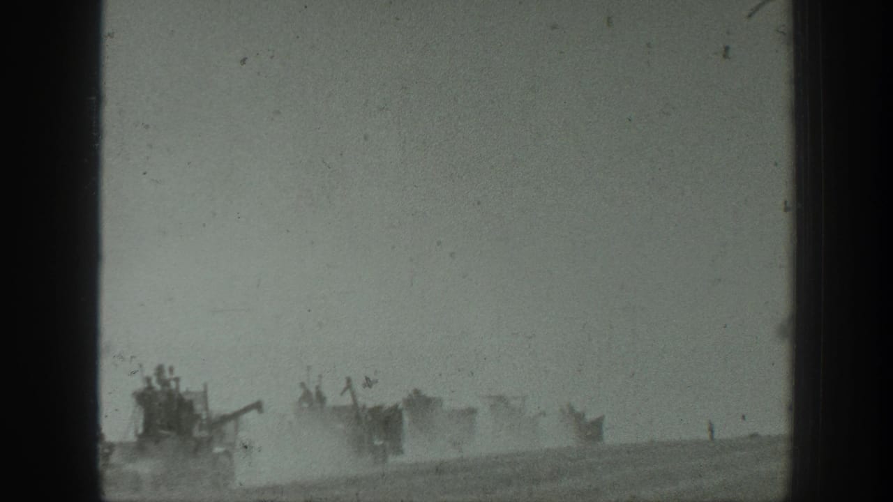 Distant armored vehicles move through a dusty open field with soldiers faintly visible on top.