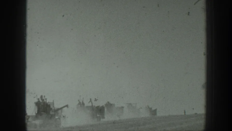 1939 California home-movie frame showing distant military vehicles crossing a dusty field with uniformed personnel riding aboard.