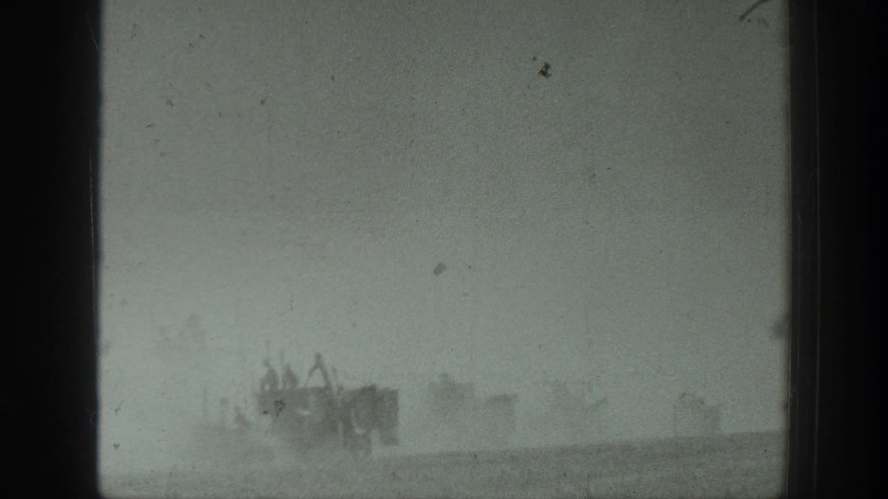 Armored vehicles and personnel appear in haze and dust along a flat horizon.