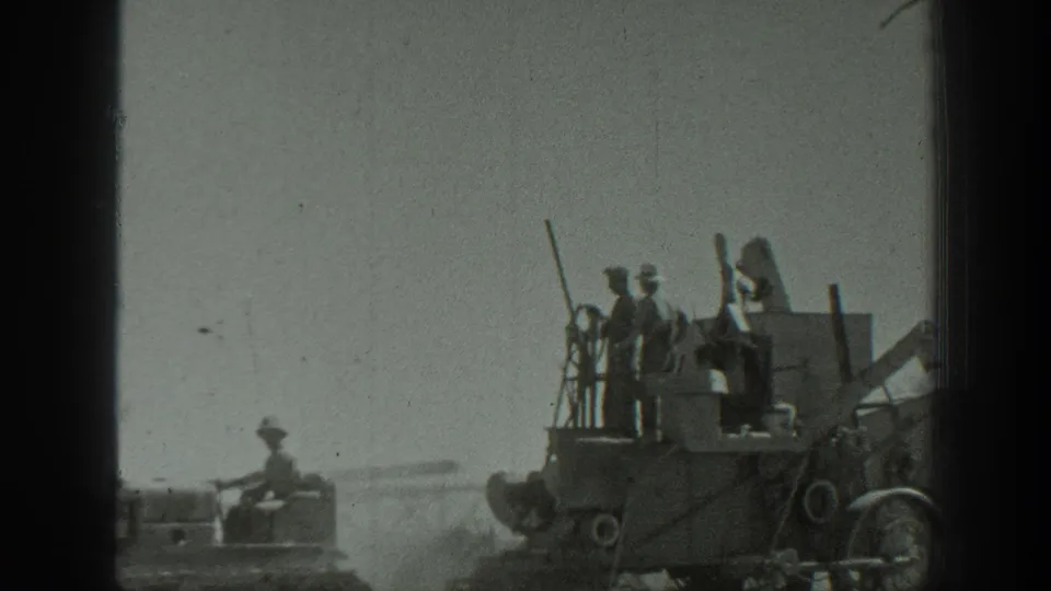 A 1939 California frame shows soldiers standing on an armored vehicle with dust trailing behind in an open field.