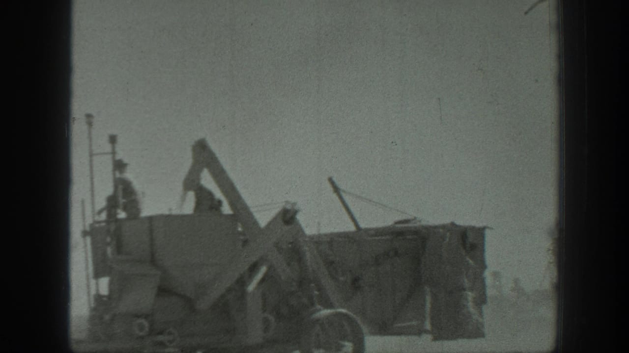 Large industrial machine or hopper with workers standing on top in a dusty outdoor setting.