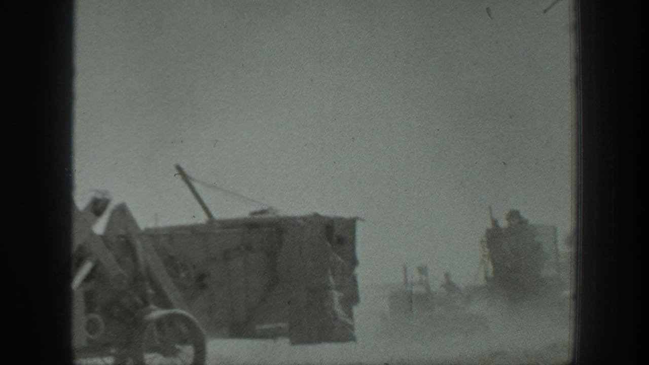 Industrial equipment moves or stands in dust, with a second vehicle visible in the background.
