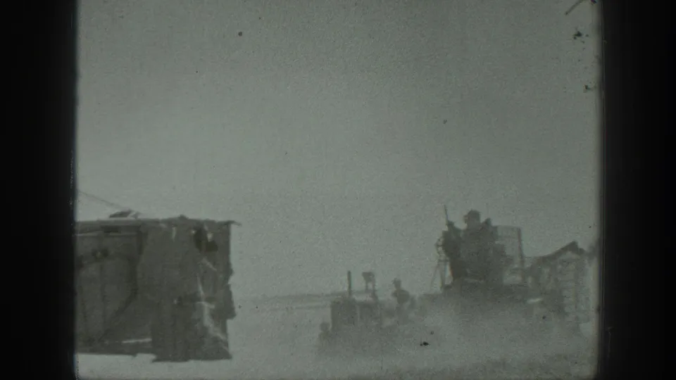 1939 California 8mm frame showing a cropped machine at left and workers around a distant vehicle in a dusty outdoor area.