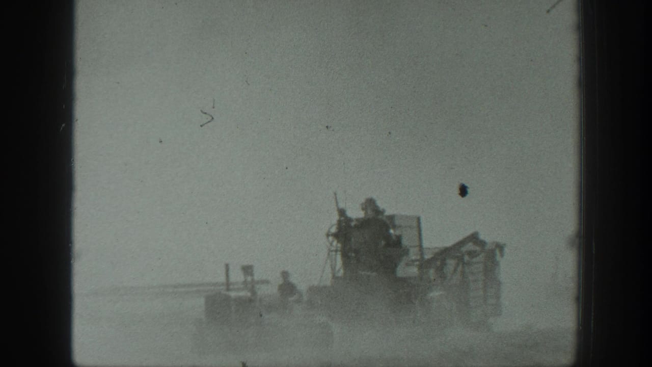 Farm machinery moves across a dusty field with workers riding on the equipment.