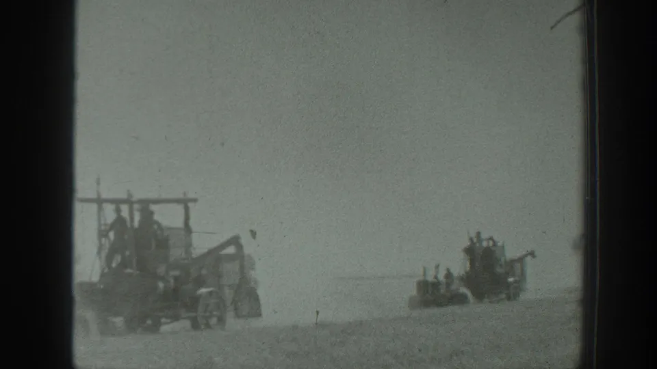 Two agricultural machines appear separated across a dusty California field, with workers riding exposed positions on the equipment.